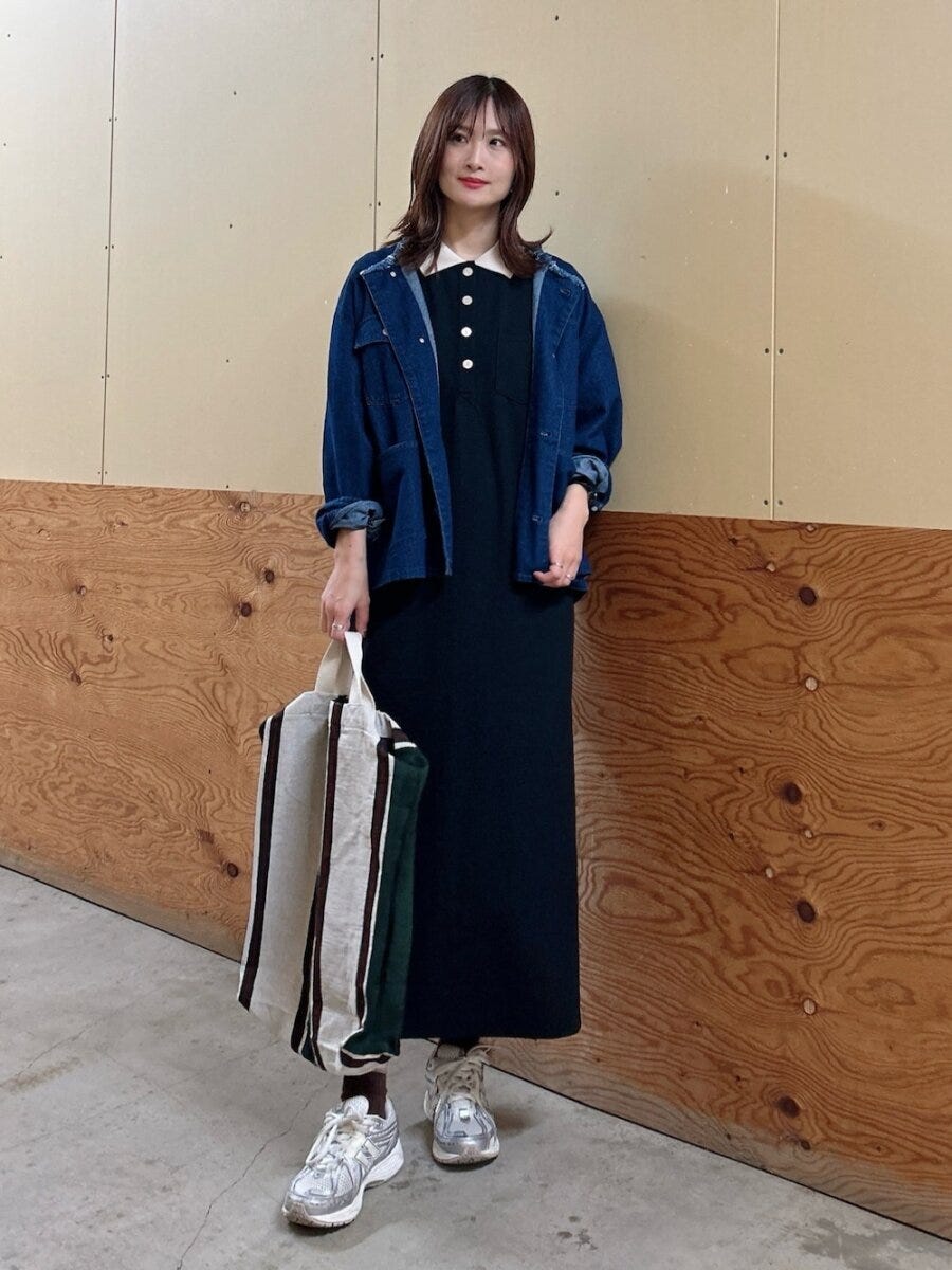 濃い青デニムジャケットと黒ワンピース、スニーカーの女性