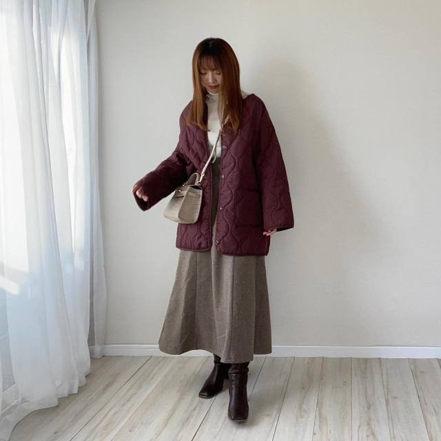 白のタートルネックニットにブラウンのキルティングジャケットを羽織り、フレアスカートを合わせスクエアブーツとベージュのショルダーバッグをコーディネート