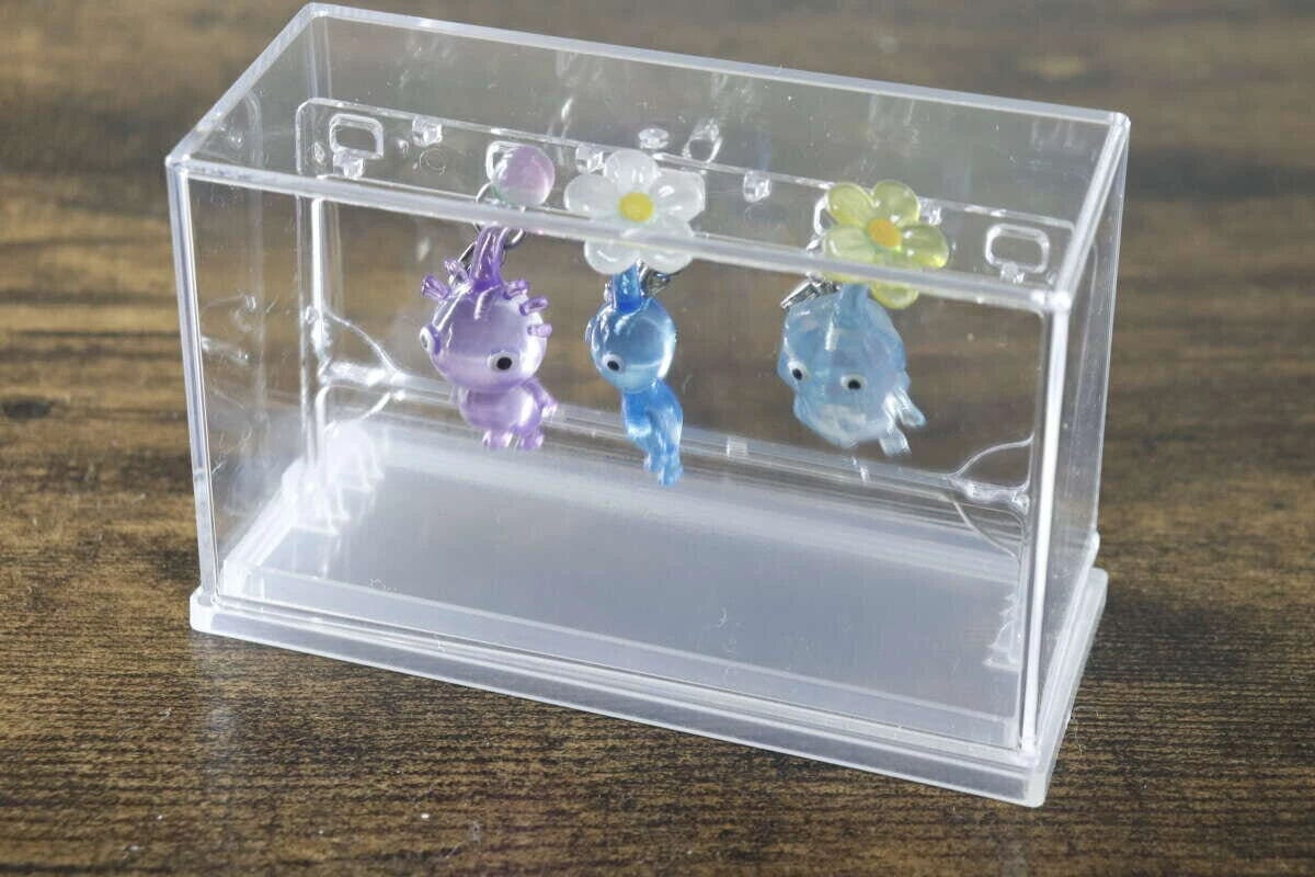 透明なミニチャームディスプレイケースの中に、3つの小さなチャームが吊るされている 透明なミニチャームディスプレイケースの中に、3つの小さなチャームが吊るされている