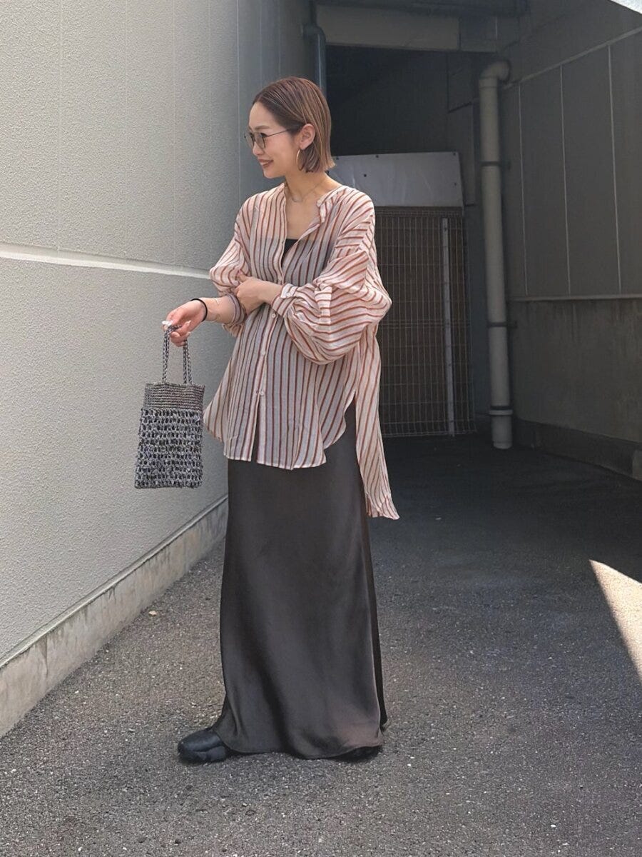 シアーストライプシャツとグレーサテンスカートを着用し、屋外に立つ女性