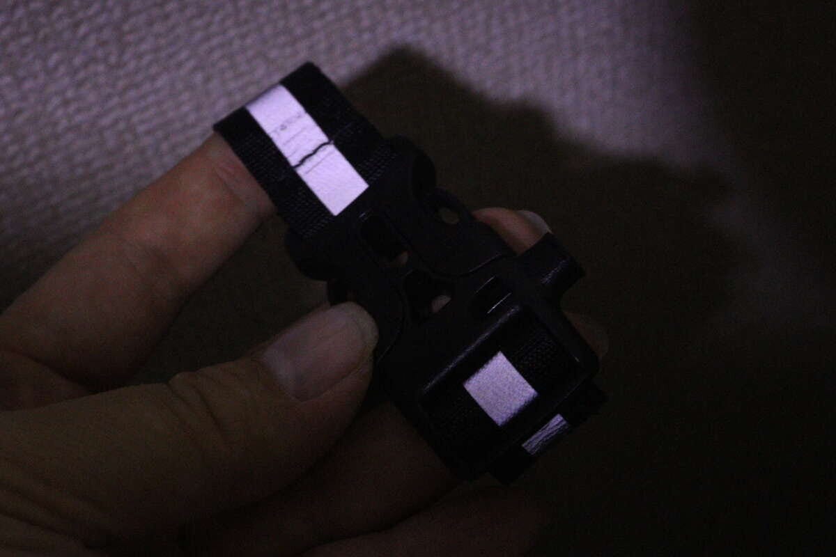暗闇で光を反射している反射材バックルを手に持っている様子 暗闇で光を反射している反射材バックルを手に持っている様子