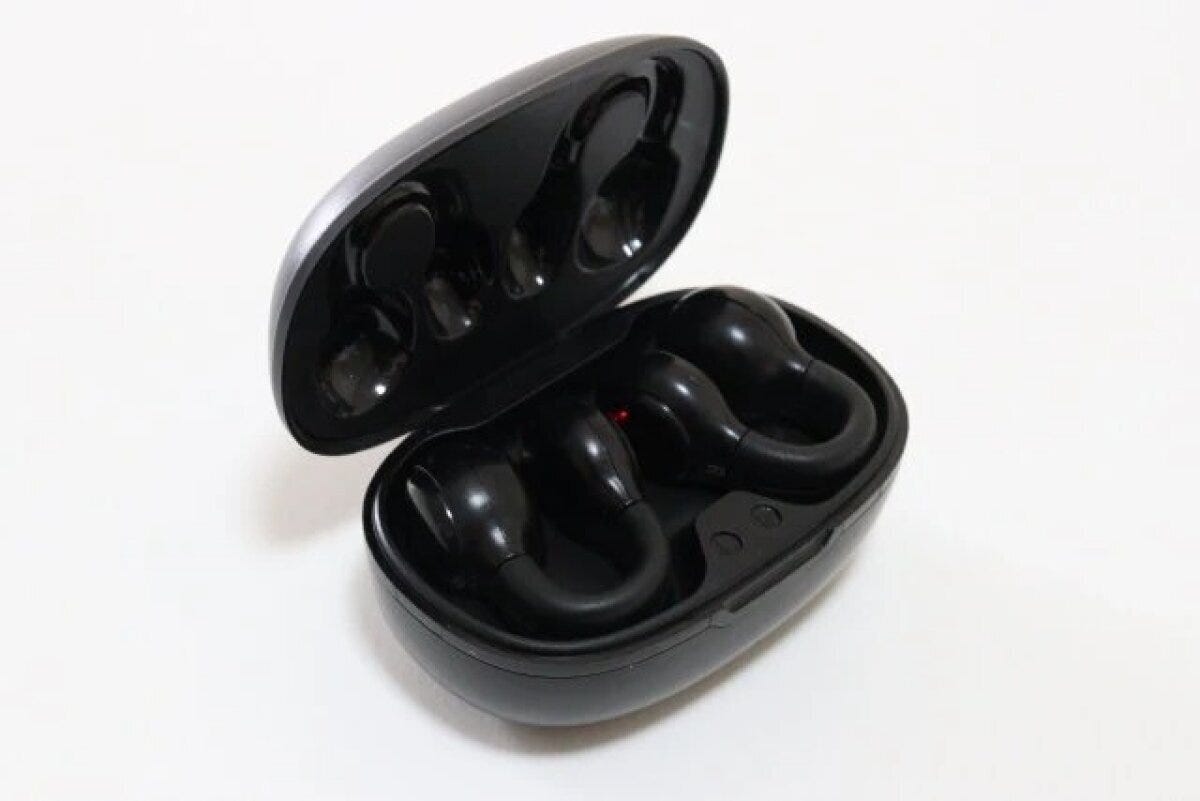 開いた黒い充電ケースに収められた耳穴をふさがないタイプのイヤホン 開いた黒い充電ケースに収められた耳穴をふさがないタイプのイヤホン