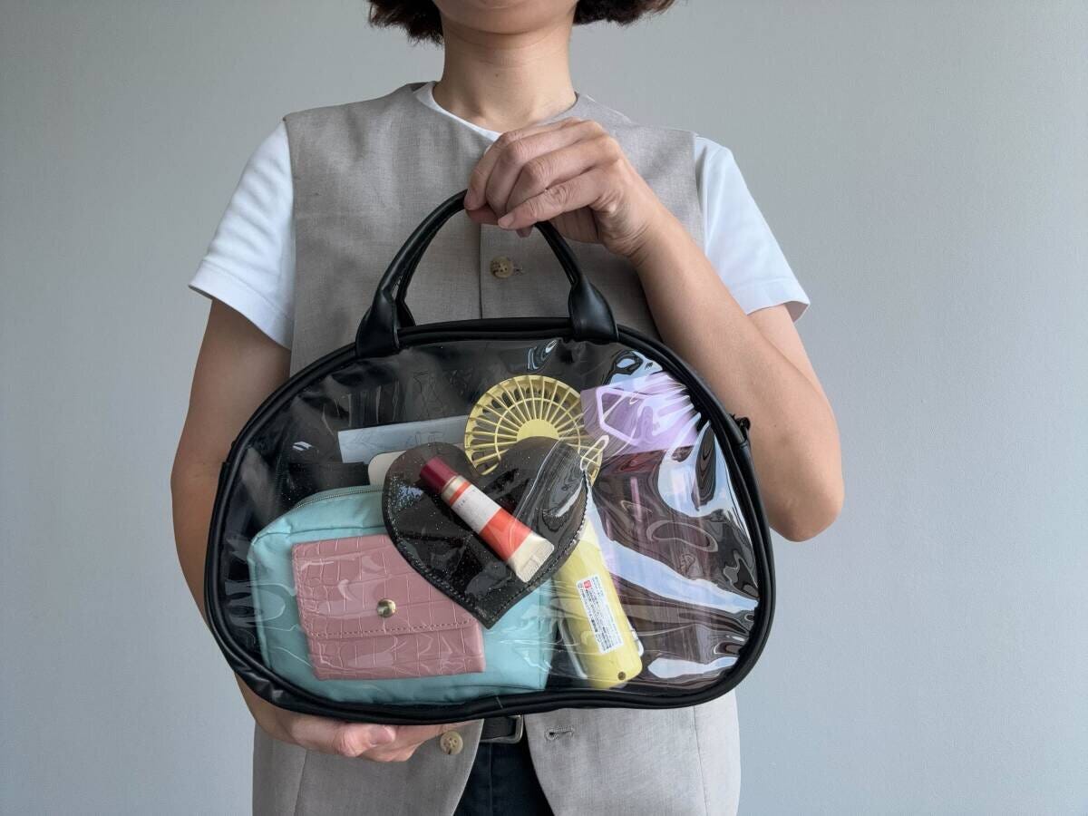 女性が黒いクリアバッグを持ち、中身の小物を見せている