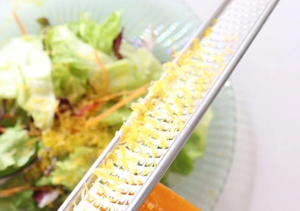 チーズグレーターでサラダの上にチーズを削りかけている様子 チーズグレーターでサラダの上にチーズを削りかけている様子
