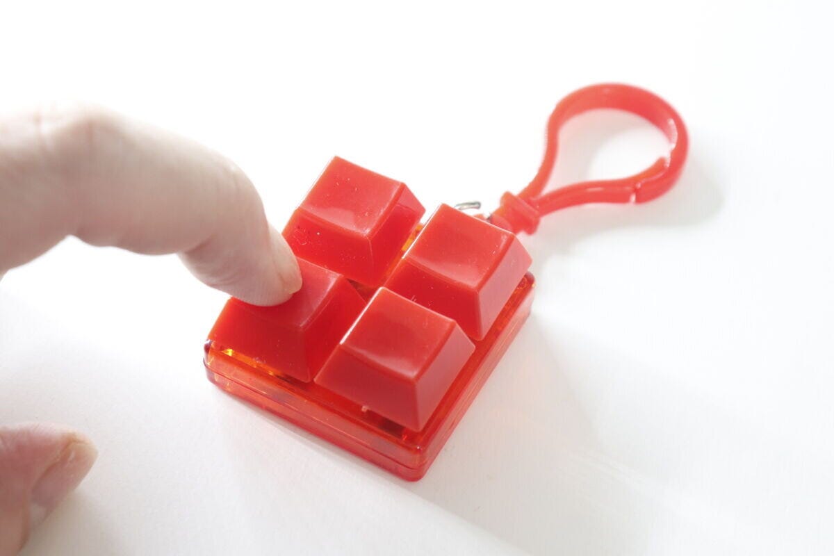 指で赤いカラーブロックキーホルダーのボタンを押し込んでいる様子 指で赤いカラーブロックキーホルダーのボタンを押し込んでいる様子