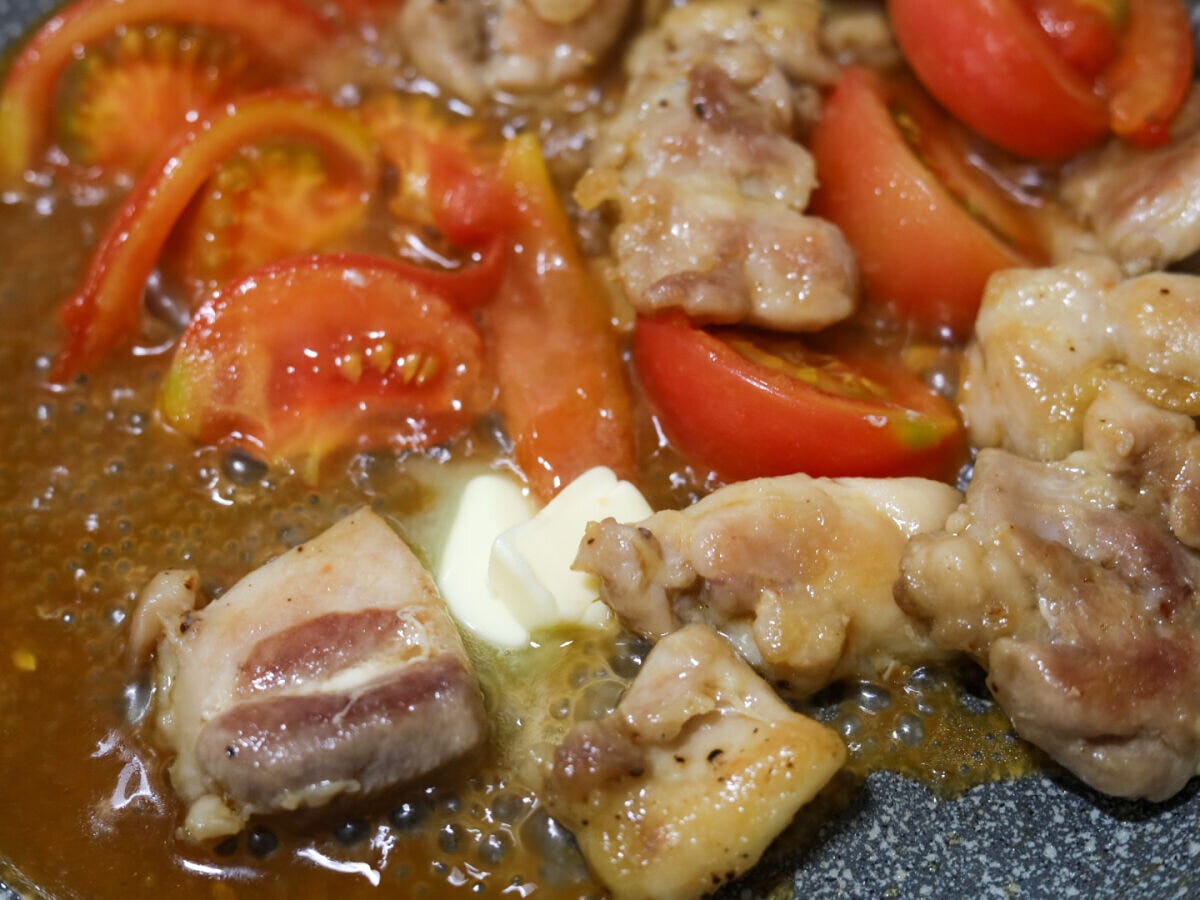 バターを加えて絡める工程 鶏もも肉とトマトを炒め合わせたフライパンにバターのかたまりを加えて溶かし絡めている様子