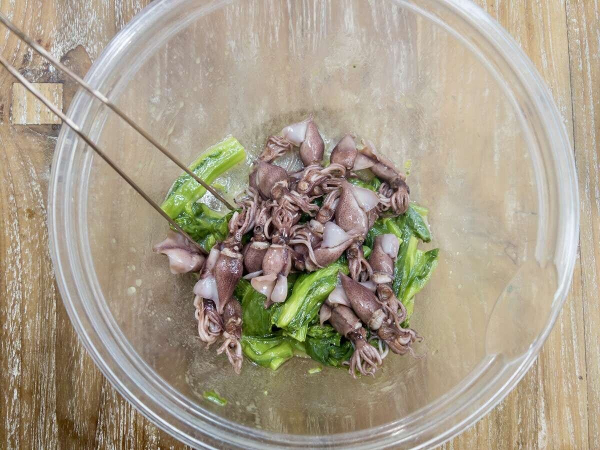 ガラスボウルで菜の花とホタルイカをトングでマリネ液と和えている工程の俯瞰写真