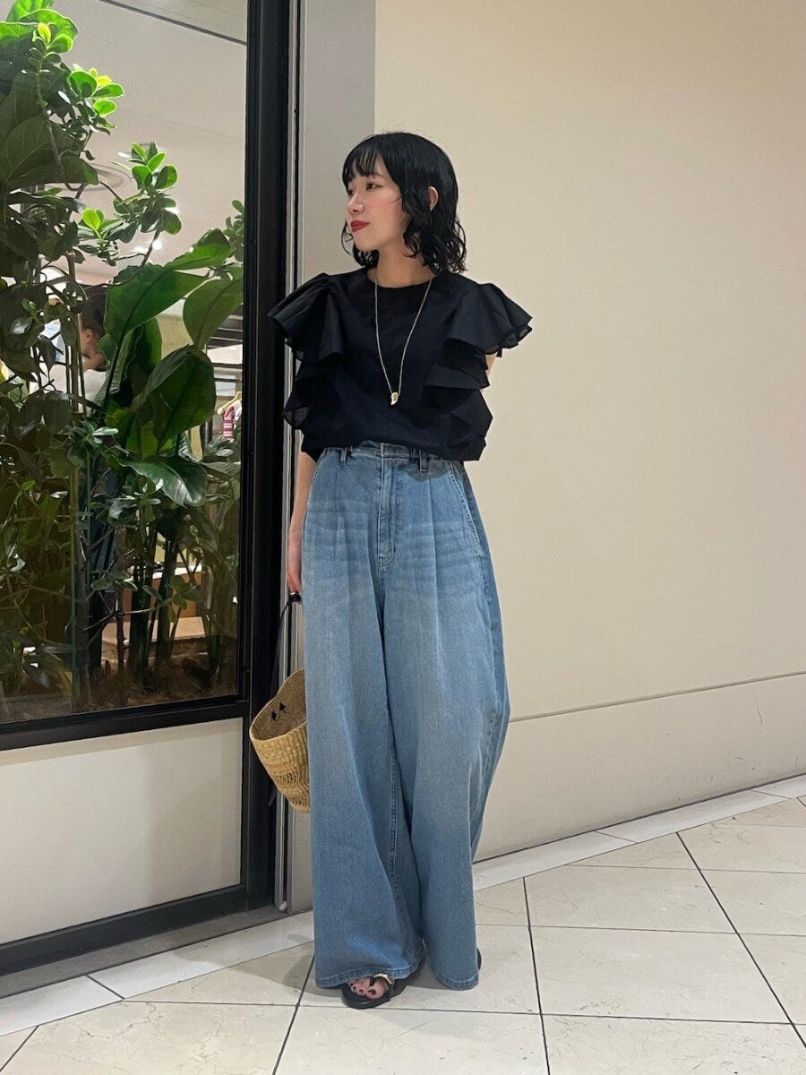 黒のフリルブラウスとワイドデニムを着用