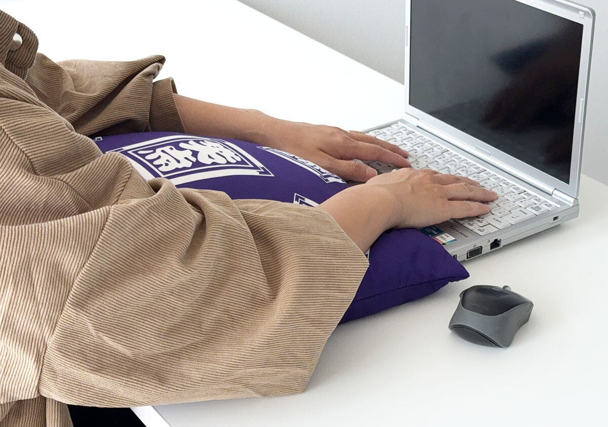 デスクに置いた笑点座布団クッションに腕を乗せてノートパソコンで作業する様子