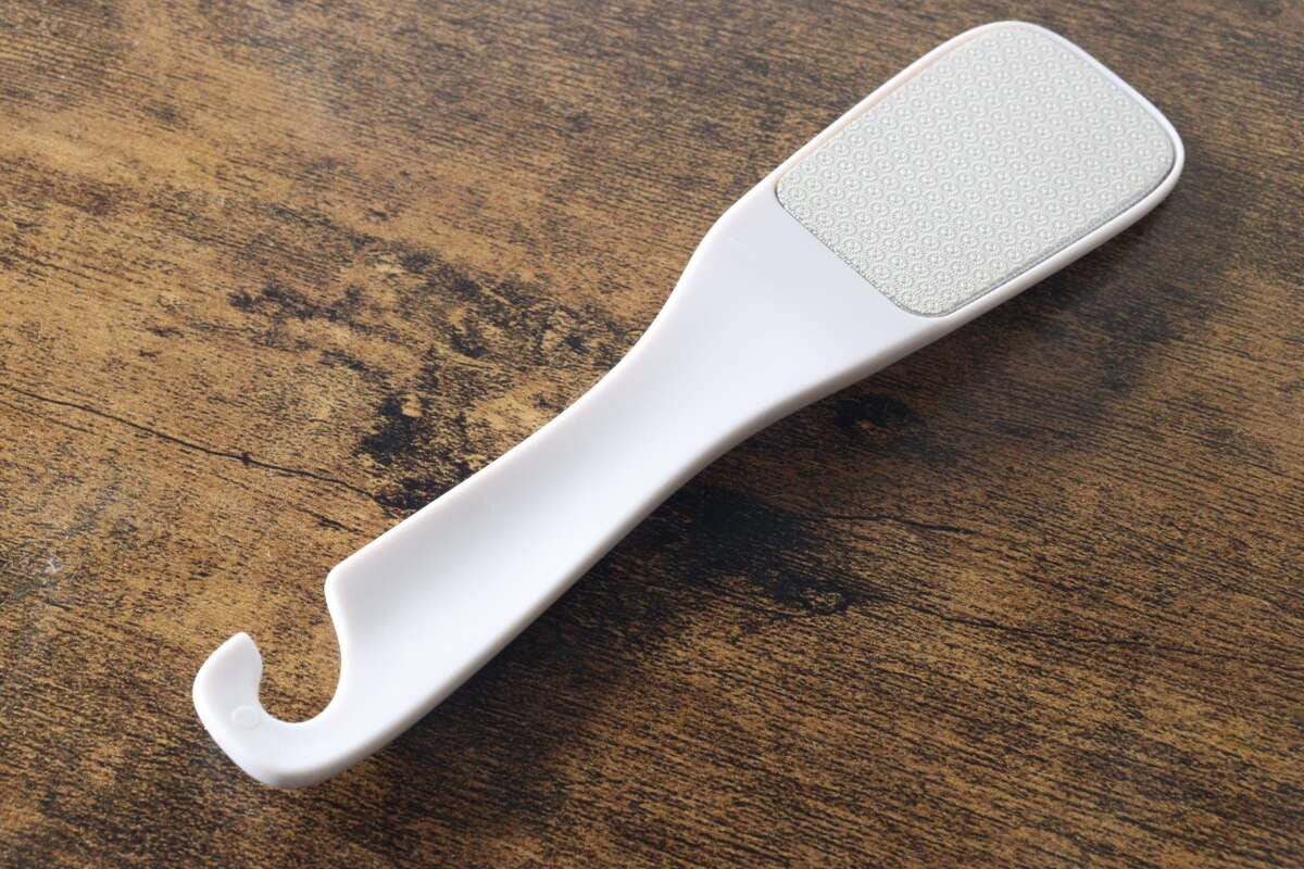 白い持ち手とグレーのやすり部分を持つダイソーのかかとやすりが木目のテーブルに置かれている斜め上からの写真