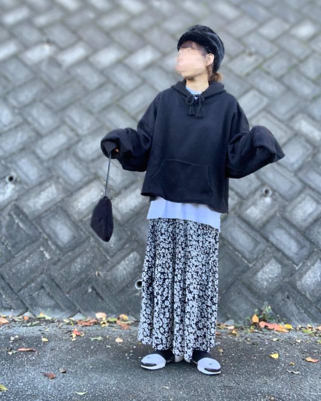 黒のパーカーに白のインナーをレイヤードし、小花柄ロングスカートを合わせ、黒の巾着バッグ、スニーカー、ベレー帽をコーディネート