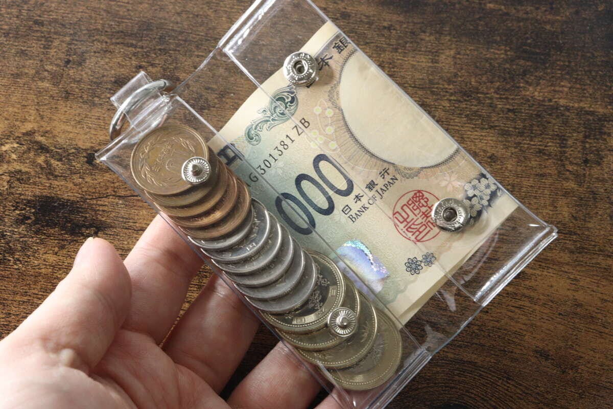 手がPVCコインポーチを持ち、中に硬貨と二つ折りの千円札が入っている