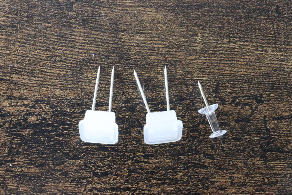 2本のピンがついた専用の白い固定具2個と通常の画鋲を並べた比較写真 2本のピンがついた専用の白い固定具2個と通常の画鋲を並べた比較写真