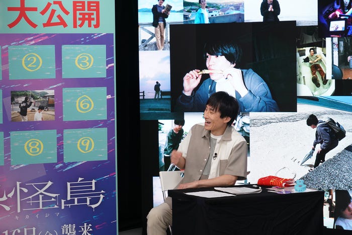 西畑大吾の写真の前で話すなだぎ武(C)2023「忌怪島/きかいじま」製作委員会