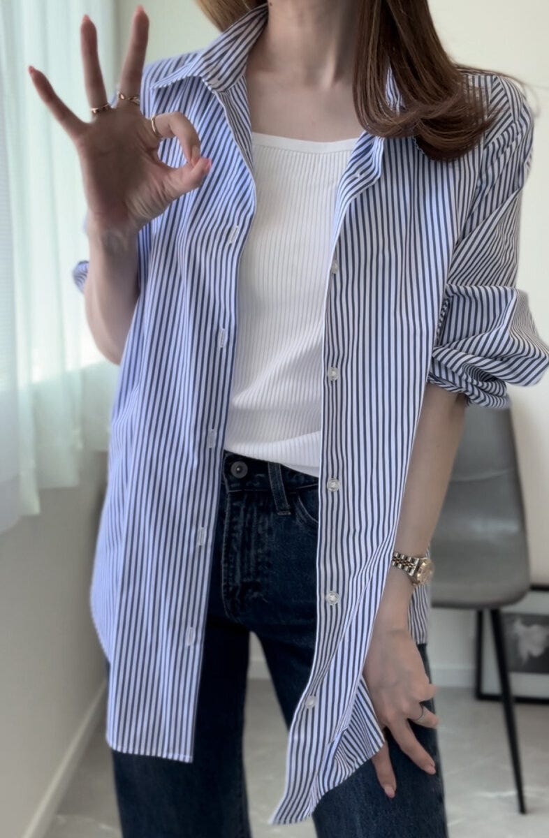 白いブラキャミにストライプシャツを羽織った女性がOKサインをしている 白いブラキャミにストライプシャツを羽織った女性がOKサインをしている