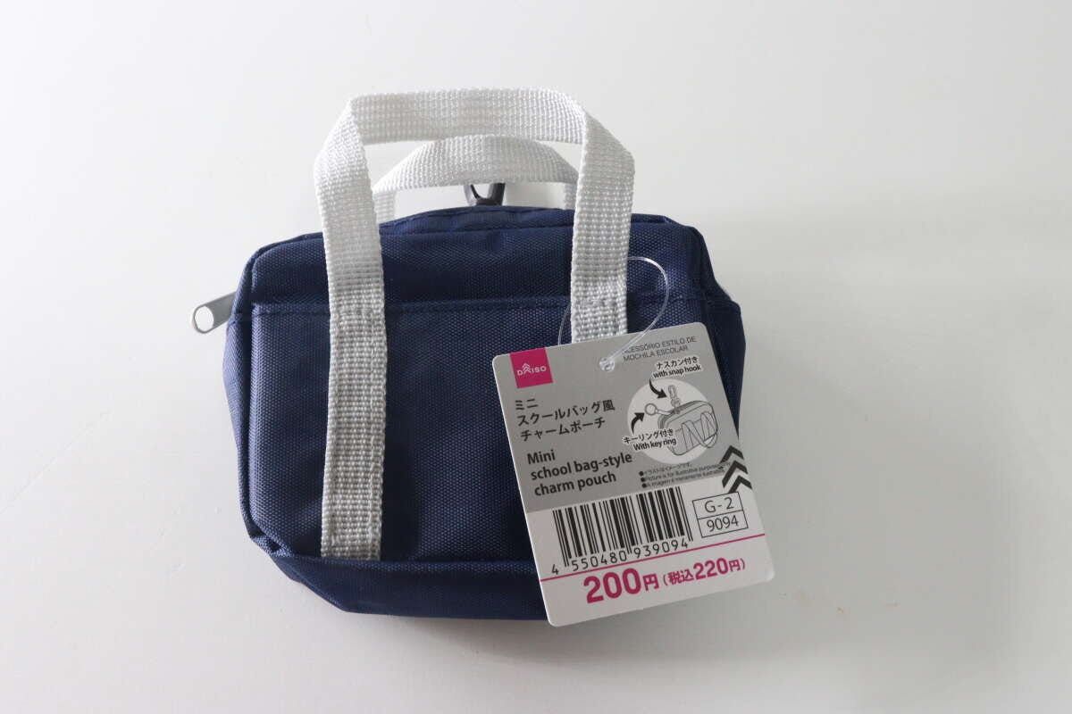 紺色のミニスクールバッグ風チャームポーチが白い背景に置かれ、商品タグが付いている 紺色のミニスクールバッグ風チャームポーチが白い背景に置かれ、商品タグが付いている