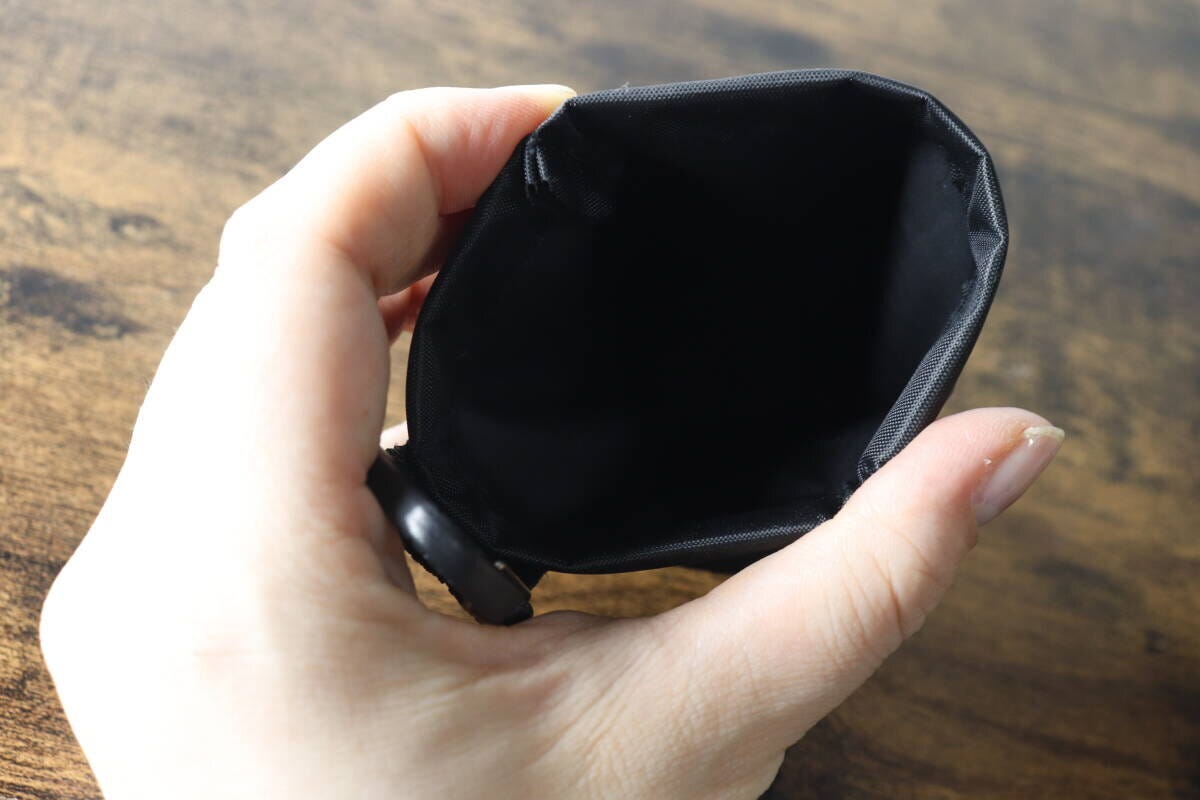 女性の手が黒い携帯ごみポーチのバネ口を開き、内側が見えている