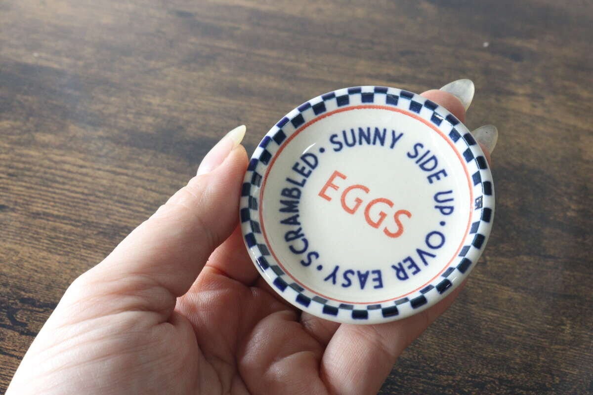 青いチェック柄とEGGSのロゴが入ったSサイズの小皿を手に持っている様子 青いチェック柄とEGGSのロゴが入ったSサイズの小皿を手に持っている様子