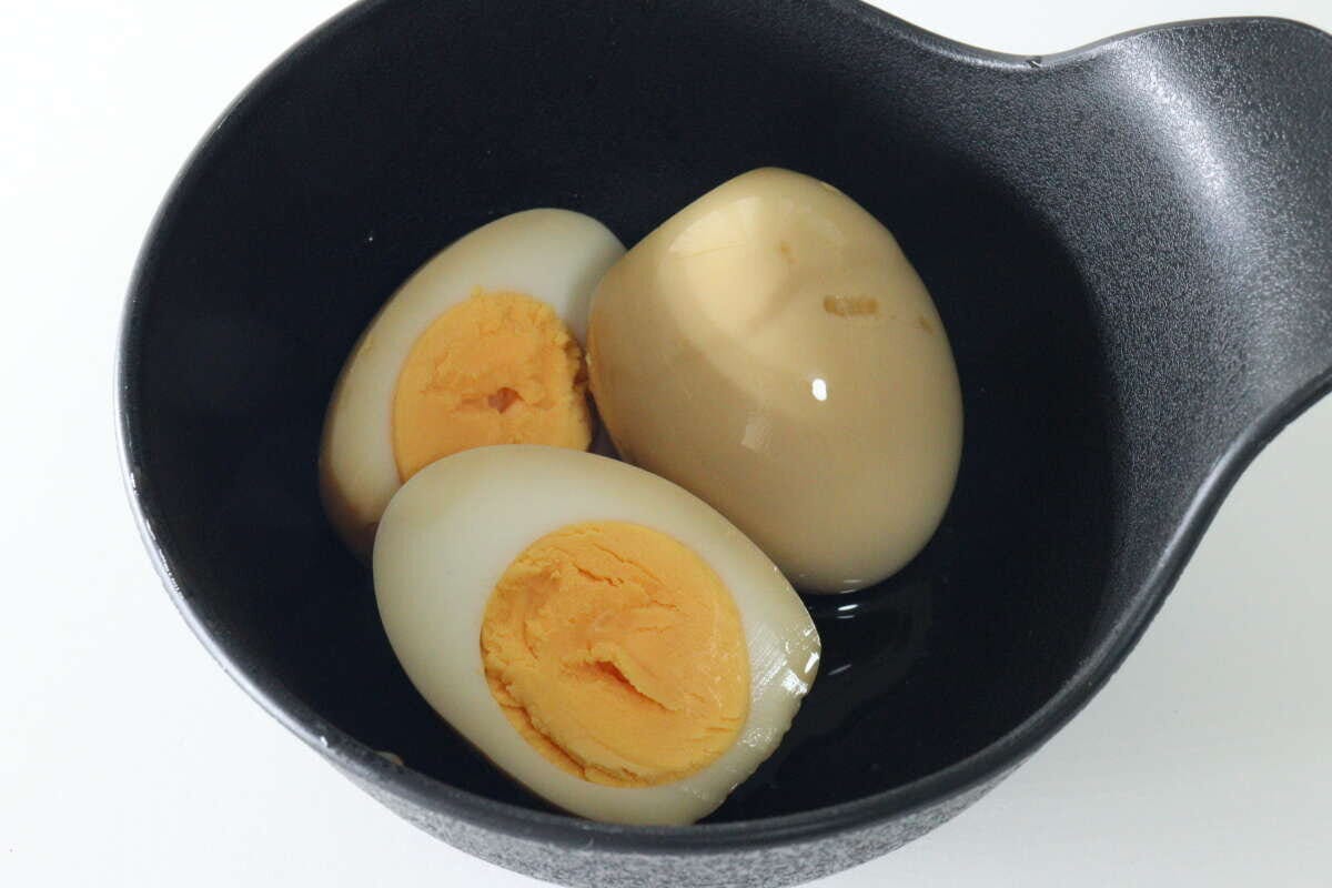 黒い器に盛り付けられた味付け玉子と半分に切った味玉 黒い器に盛り付けられた味付け玉子と半分に切った味玉