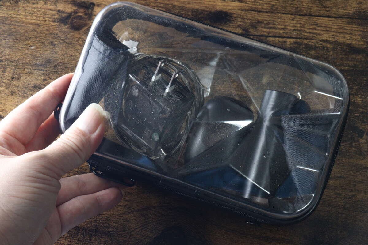 女性の手が透明なダイヤモンド形収納バッグを持ち、中にモバイルバッテリーとワイヤレスイヤホンが入っている 女性の手が透明なダイヤモンド形収納バッグを持ち、中にモバイルバッテリーとワイヤレスイヤホンが入っている