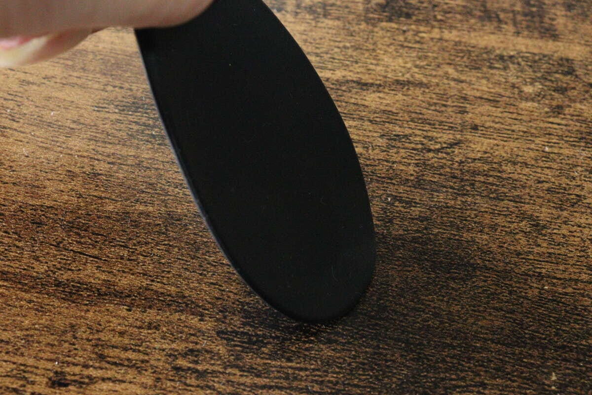 黒いシリコーンスプーンの先端部分が木目のテーブルに押し当てられ、しなっている様子