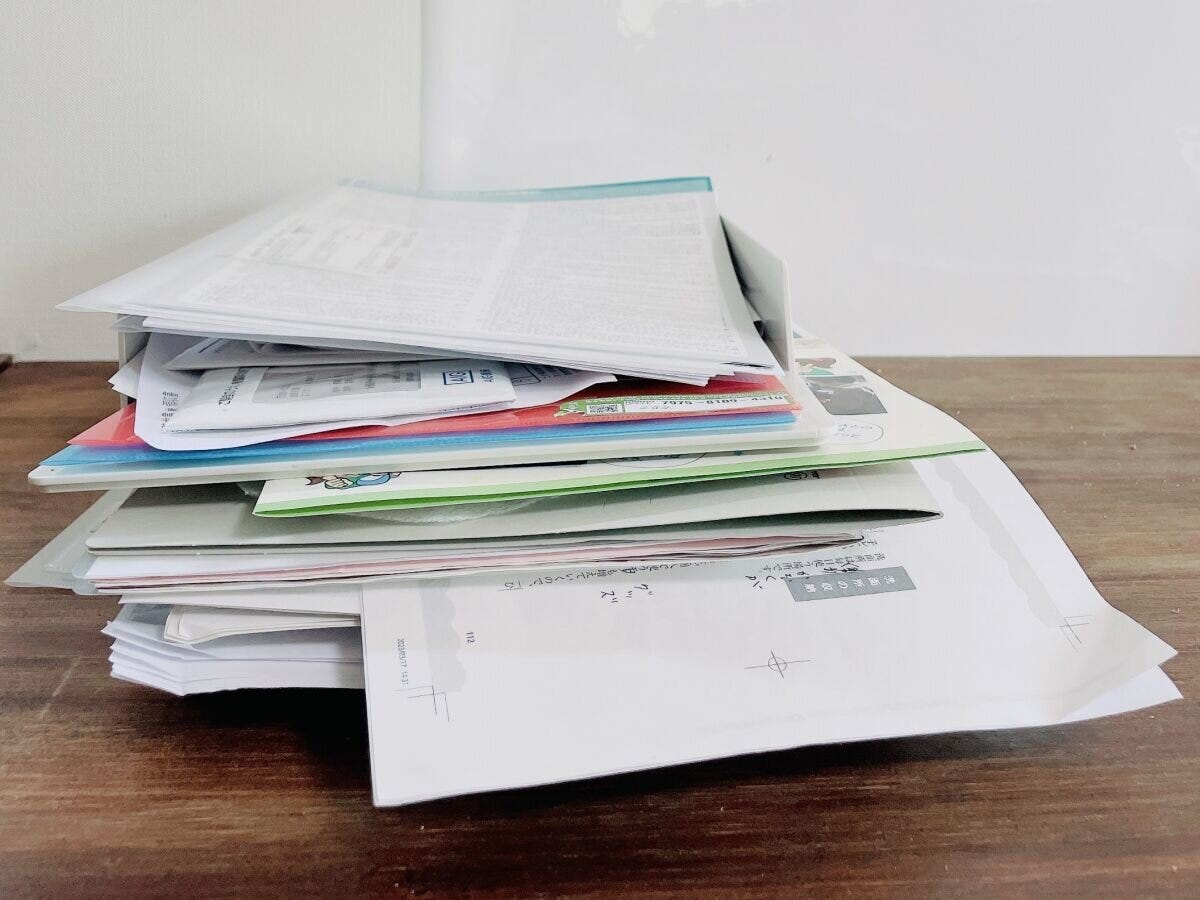 木目のテーブルに積み重なった大量の書類と封筒 木目のテーブルに積み重なった大量の書類と封筒