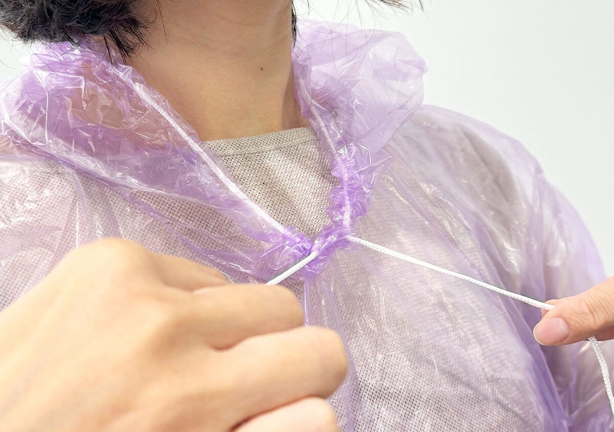 着用したレインコートの首元の紐を両手で調整している様子