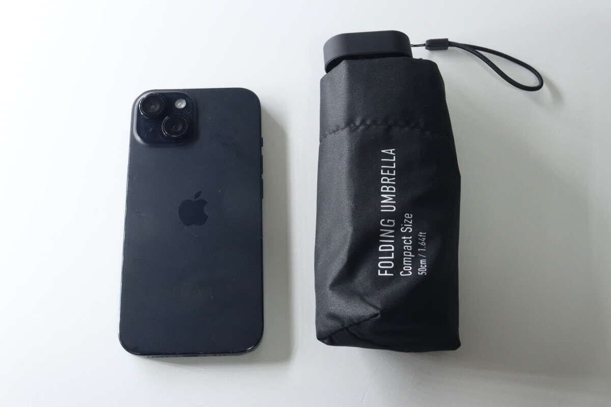 黒い折りたたみ傘とスマートフォンを並べ、コンパクトなサイズ感を比較している