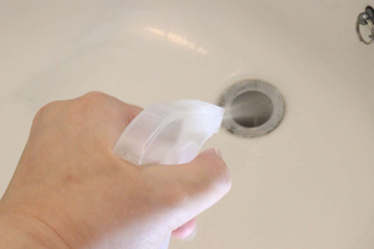 洗面台の排水口付近の汚れにスプレー容器に入れた洗浄液を噴霧している手元