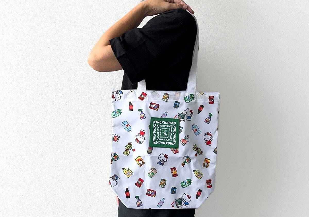 黒い服を着た人が白地の紀ノ国屋×ハローキティ保冷・保温バッグを肩にかけている