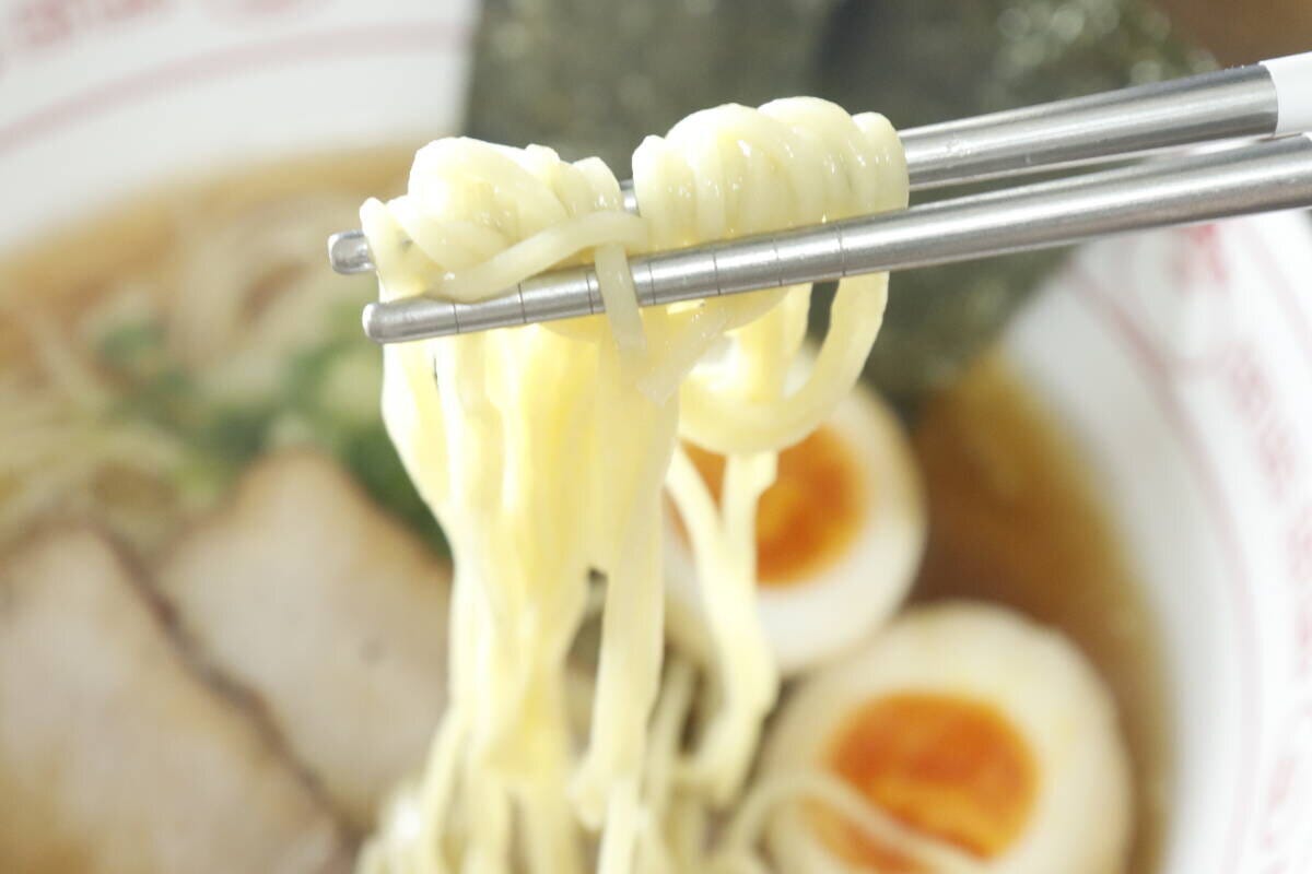 箸で持ち上げられたラーメンの麺のアップ。奥にはチャーシューと煮卵 箸で持ち上げられたラーメンの麺のアップ。奥にはチャーシューと煮卵