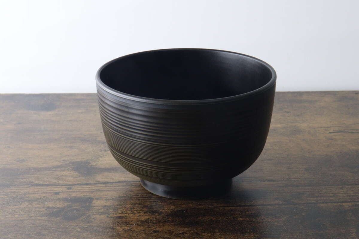 木目のテーブルに置かれたこげ茶色の汁椀