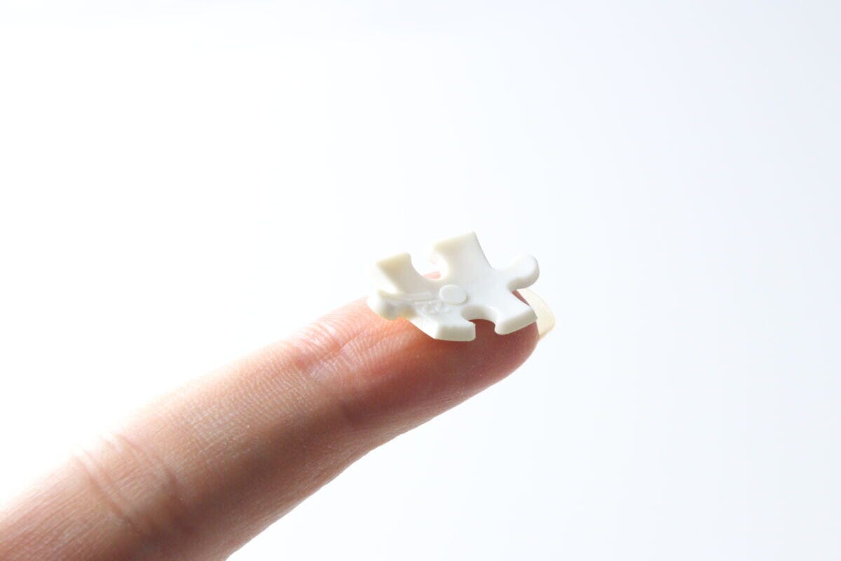 指先に小さな白いパズルピースが乗っている。ピースの裏面にはナンバーが書かれている。