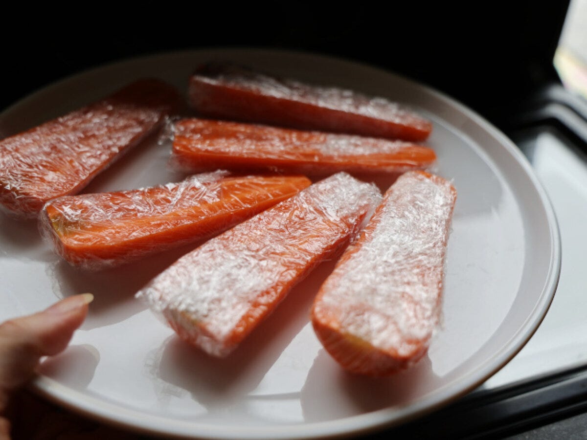 ラップで包んだにんじんを並べた皿 白い皿に縦半分に切ってラップでぴったり包んだにんじん6本を並べている写真