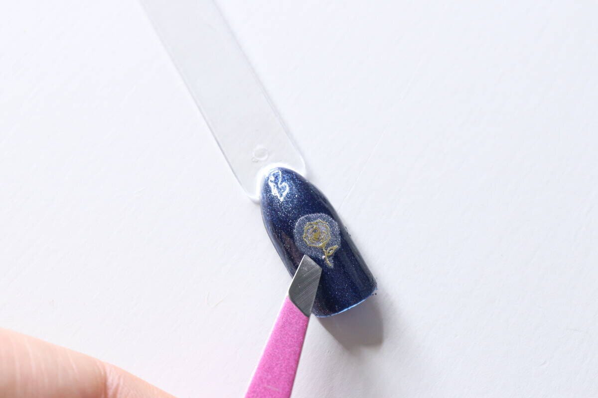 濃いブルーのネイルチップにピンセットを使って薔薇のフィルムを乗せている作業中 濃いブルーのネイルチップにピンセットを使って薔薇のフィルムを乗せている作業中