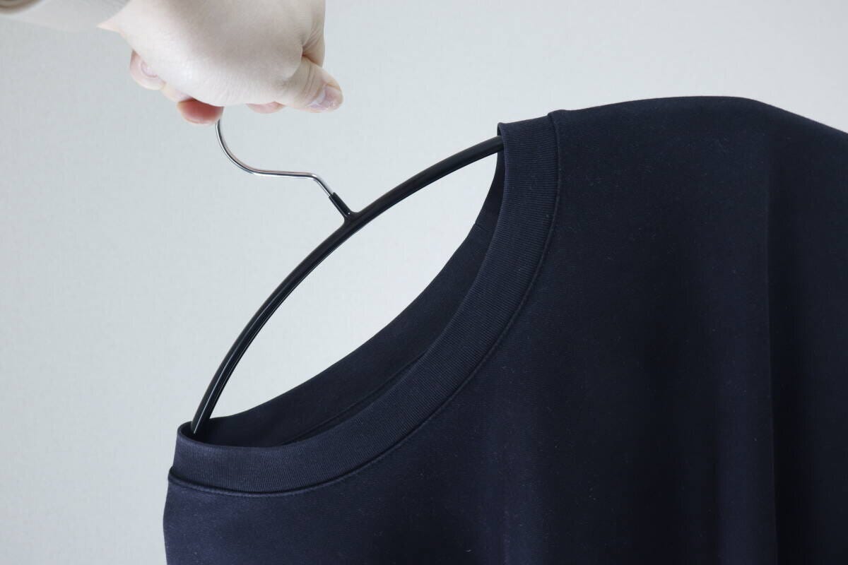黒いTシャツの首元にハンガーを差し込んでいる手元