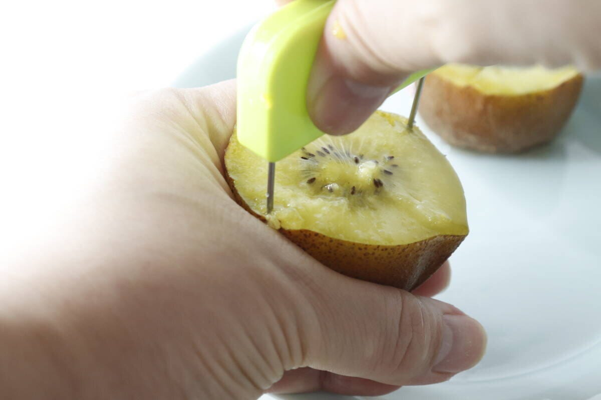 キウイに皮むき器を差し込み、皮に沿って回転させている手元