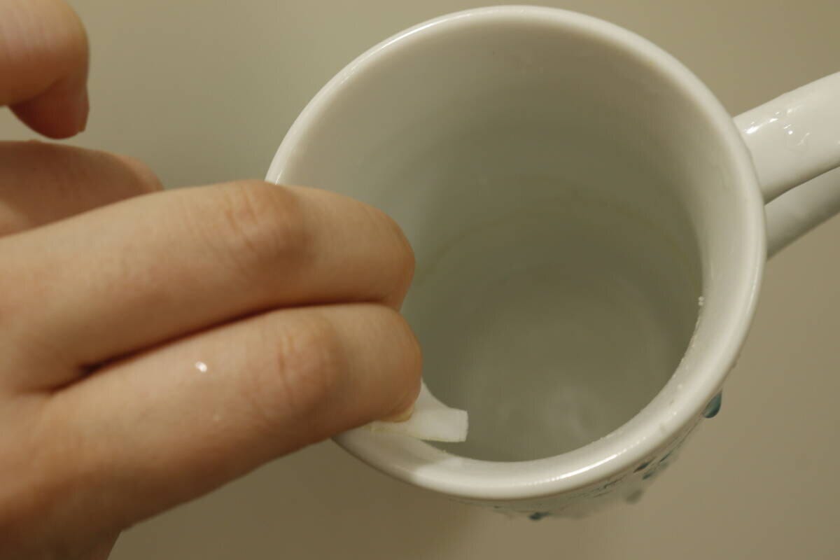 手が白いメラミンスポンジで、白いマグカップの茶渋を擦って掃除している様子