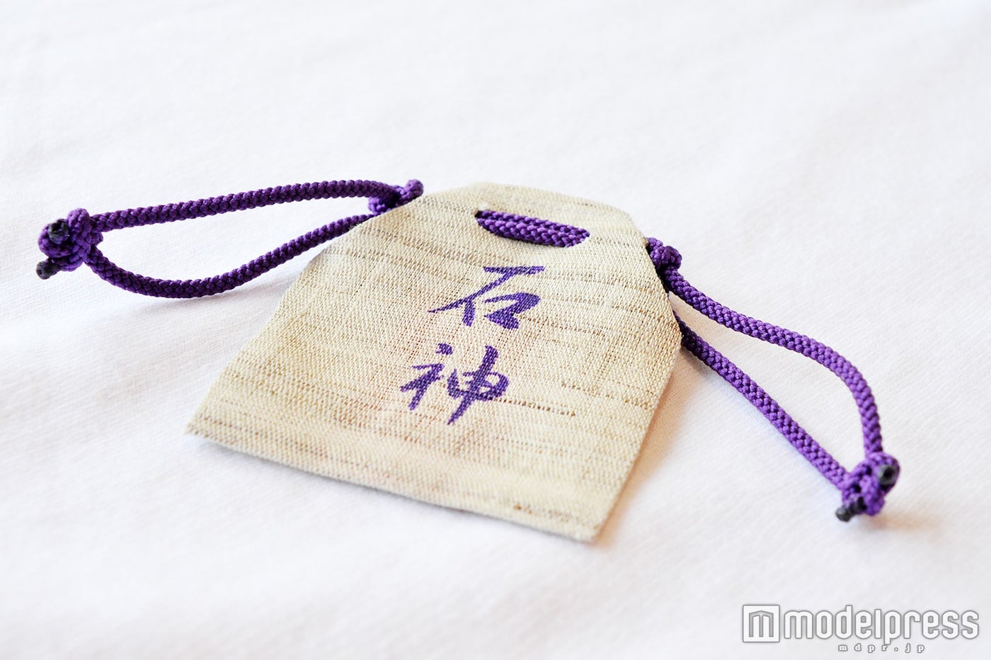 「神明神社」のお守り／麻布に貝紫色の文字書きと紐が結ばれている（C）モデルプレス