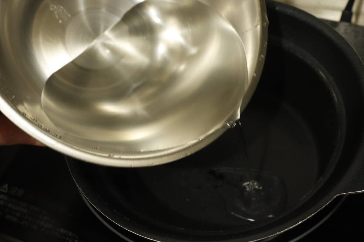 ステンレスボウルに入った水を黒い鍋に注ぎ入れている手元