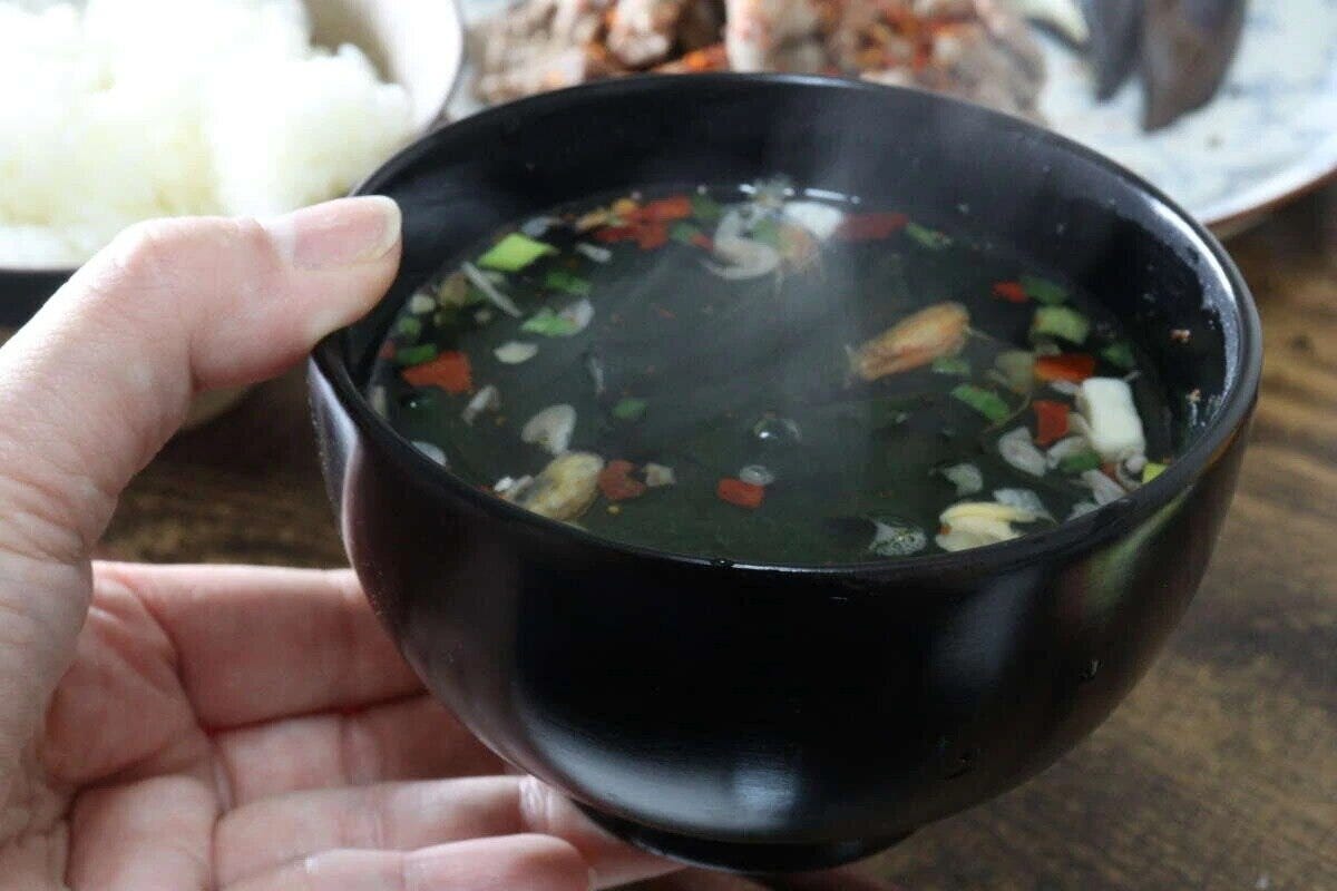 手に持った黒い京型椀に入った、湯気の立つ具だくさんの汁物