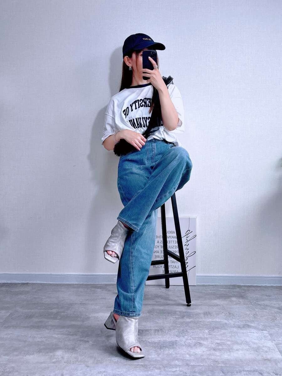 白Tシャツと水色デニムを着た女性が椅子に座りスマホを見ている