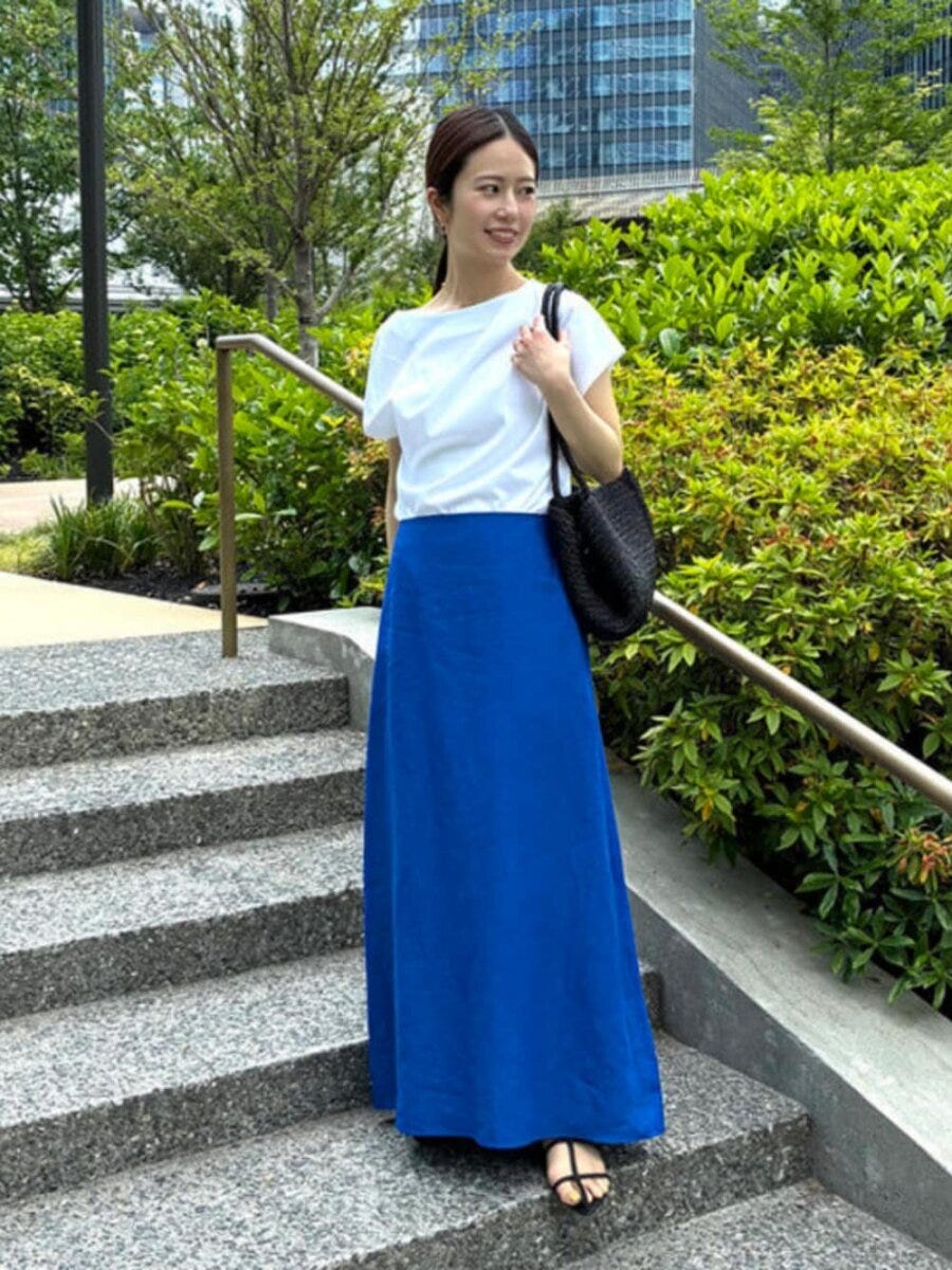 青ロングスカートと白Tを着た女性が屋外の階段で横を向く