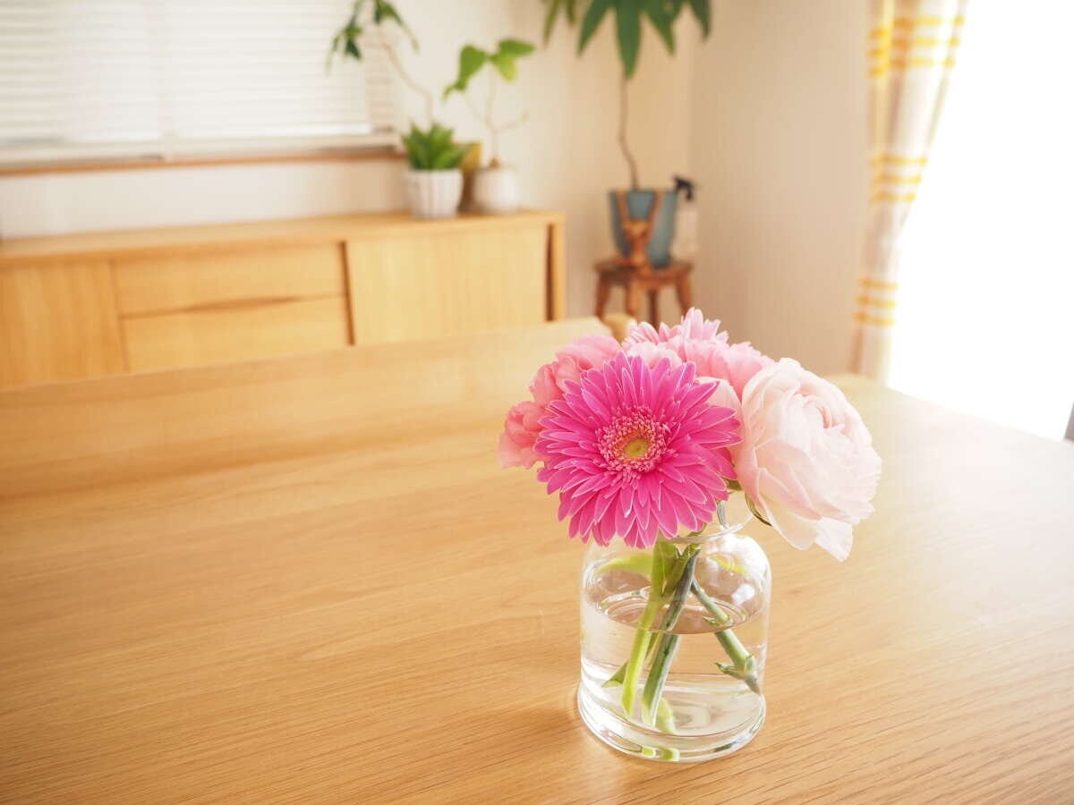 木目のテーブルにピンクのガーベラとラナンキュラスが生けられたガラスの花瓶