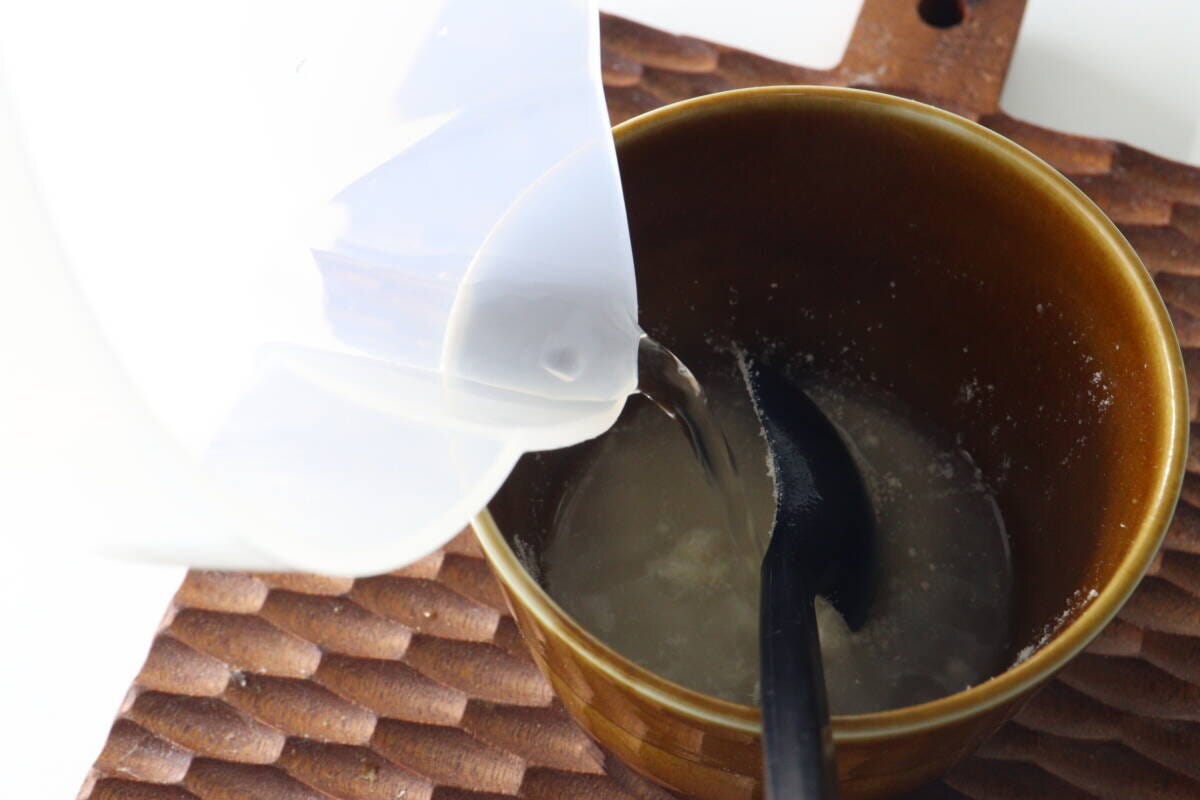 茶色のカップに入ったポタージュ粉末に、白い容器からお湯を注ぐ様子