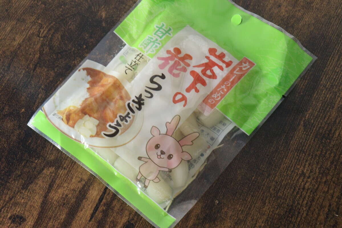 緑色のパッケージに入った岩下のカレーのための花らっきょうが木目のテーブルに置かれている 緑色のパッケージに入った岩下のカレーのための花らっきょうが木目のテーブルに置かれている