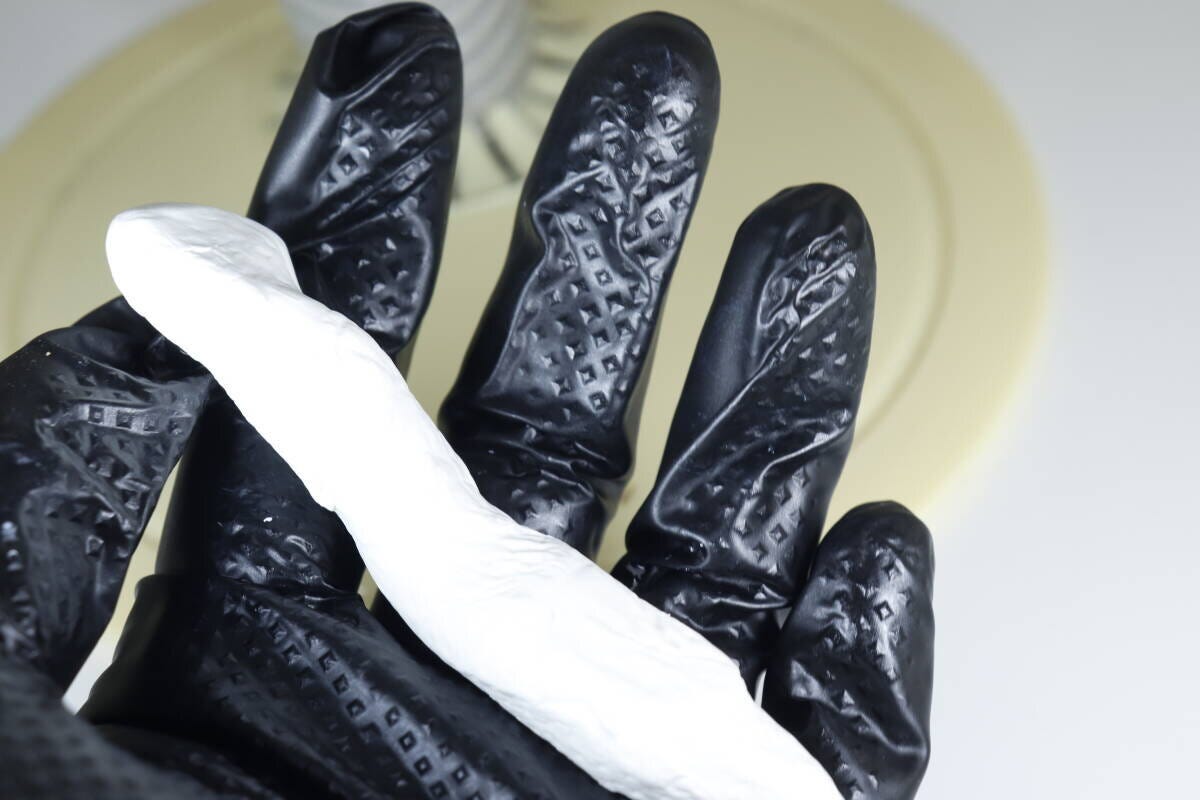 黒いゴム手袋をはめた手のひらに細長く練られた白いすきまパテ 黒いゴム手袋をはめた手のひらに細長く練られた白いすきまパテ