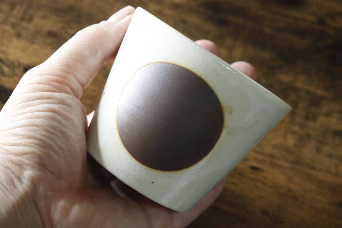 白地に茶色の丸紋があるそばちょこを手に持っている