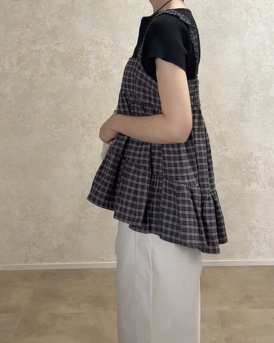 黒Tシャツと白パンツにチェックキャミを重ね着した女性が横向きに立っている