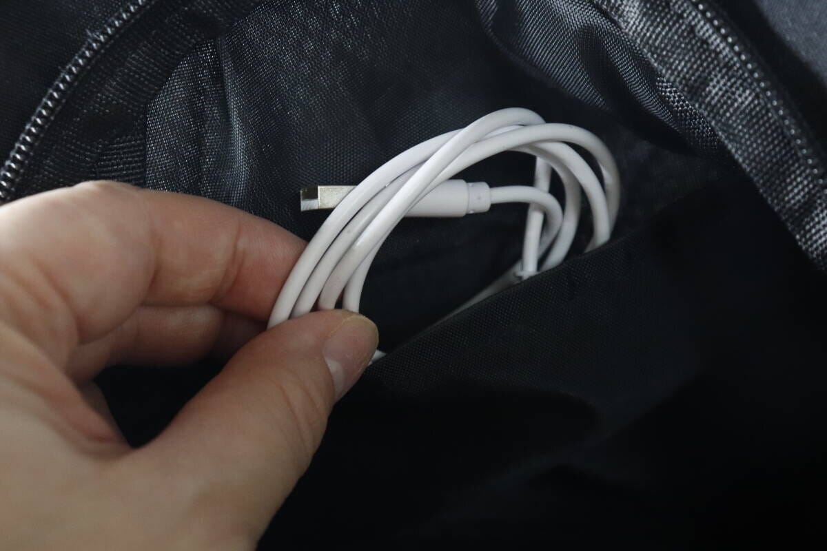 バッグの内ポケットに白い充電ケーブルを入れている手